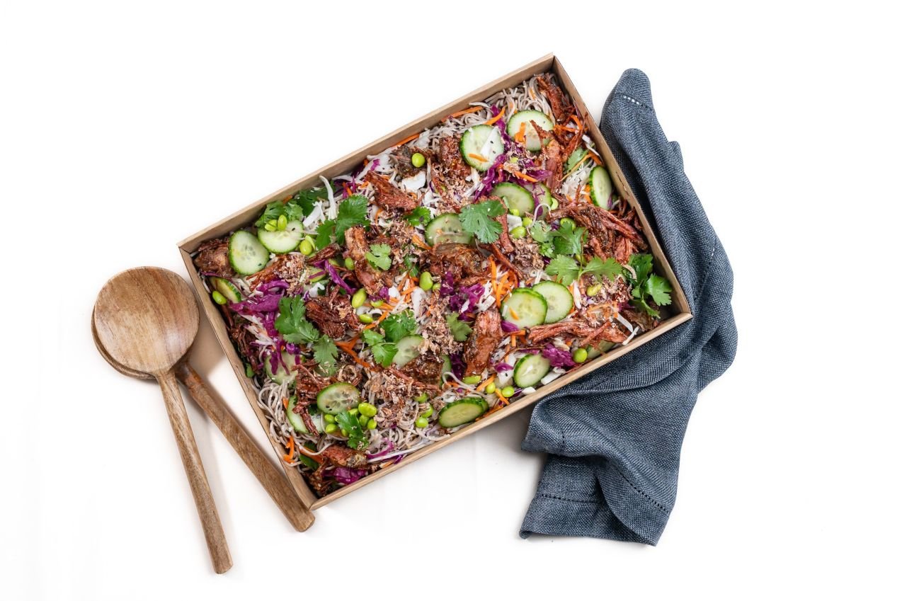 Beef brisket soba noodle salad with cucumber, cabbage, edamame, carrot and coriander in a catering box.