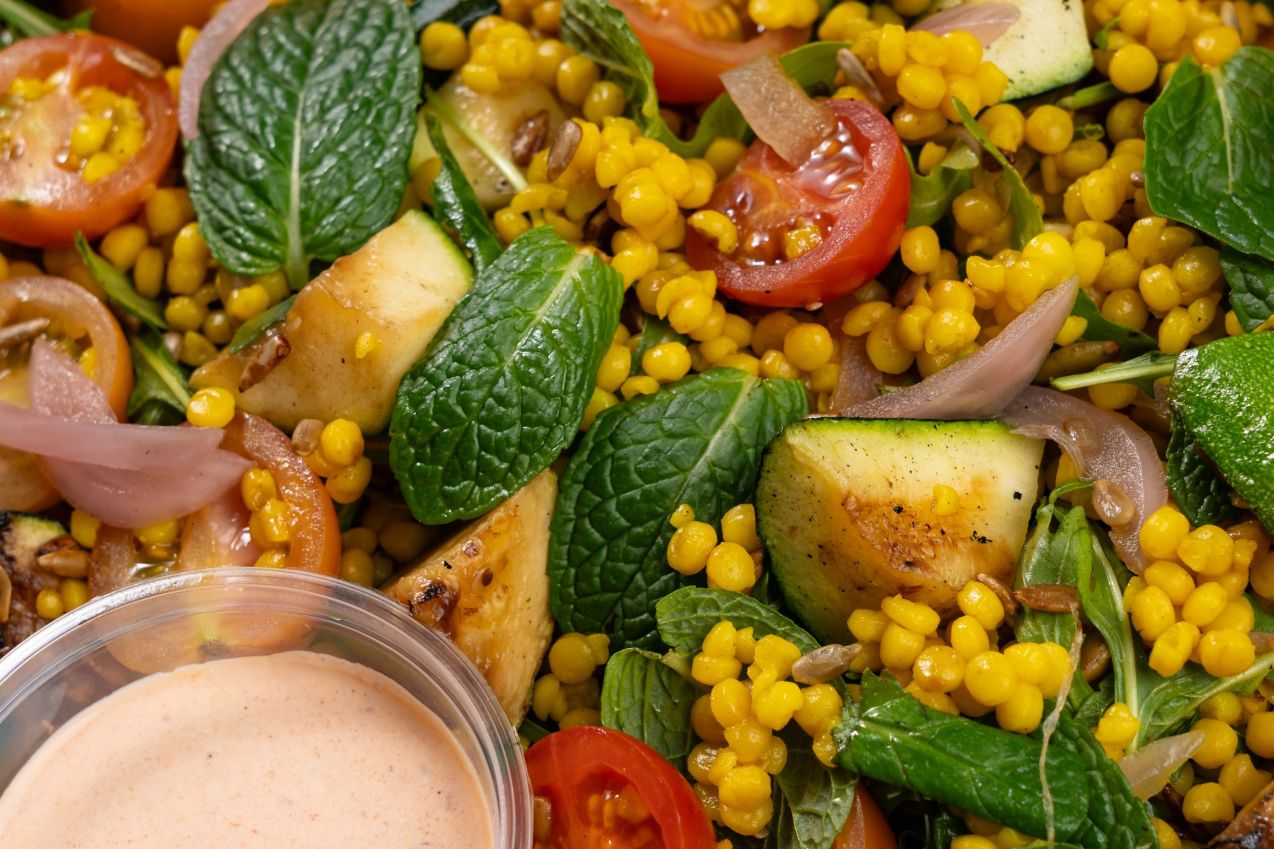 Turmeric pearl couscous salad with zucchini, tomatoes, pickled onion, roquette and herbs in a catering box.