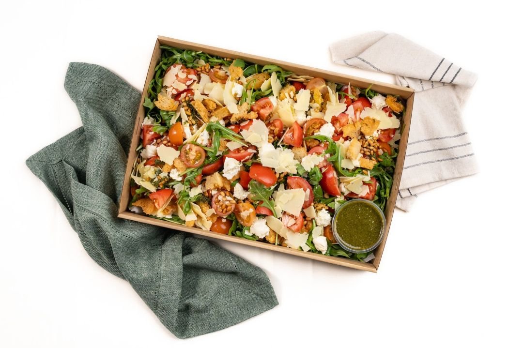 Tomato and bocconcini salad with roquette, croutons, parmesan and pesto in a shared catering box.