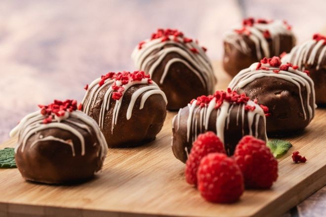 CHOCOLATE PROFITEROLES filled with fresh cream, dipped in chocolate & decorated in white chocolate drizzle & freeze dried raspberries (2 per person)