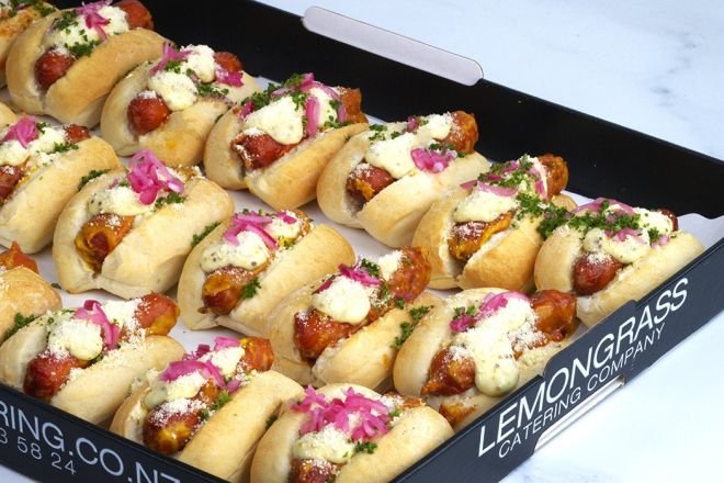 BABY AMERICAN HOT DOGS with kransky sausage topped with tomato sauce, mustard mayo, grated parmesan and sliced pickled red onion in dinner roll - served warm 