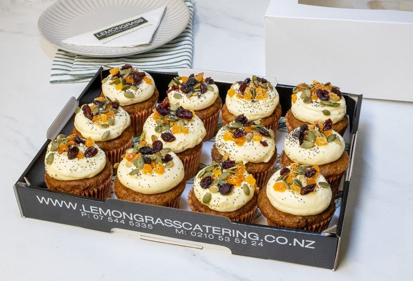 CARROT CAKE CUPCAKES  with chopped walnuts, decorated with zesty cream cheese icing topped with dried apricots, pumpkin seeds & dried cranberries - presented on black biodegradable platter