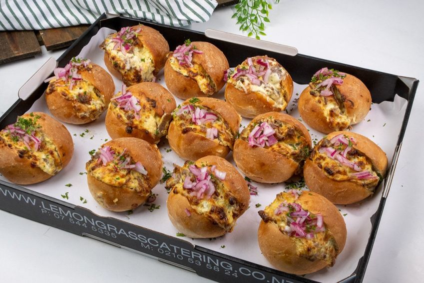 PHILLY-STYLE SHREDDED BEEF MELT with rich cream cheese, cheddar, caramelized onions in soft round midi roll topped with pickled red onions & heated in oven - served hot